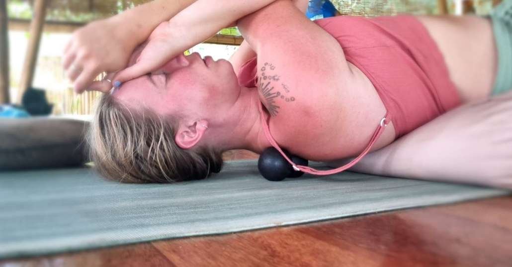 Student in supine position using black massage ball under shoulder blade on