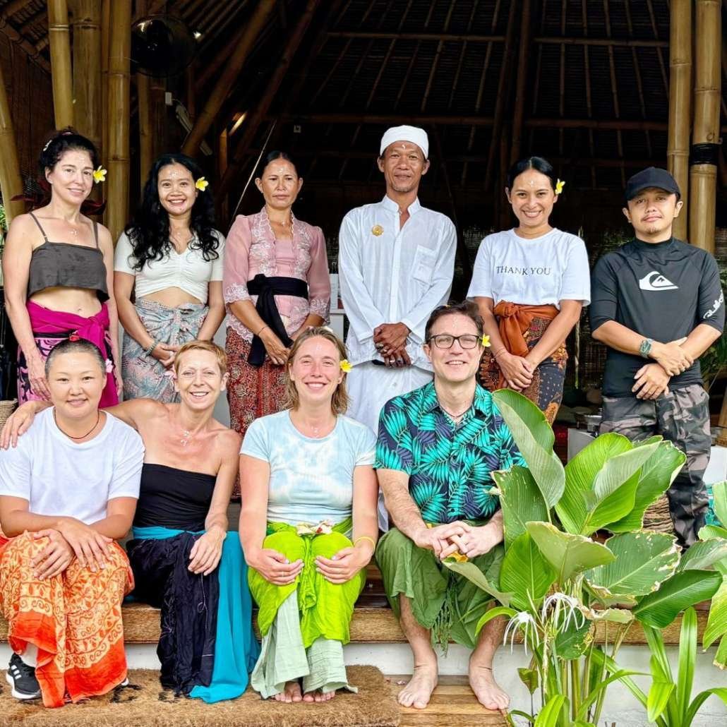Group of yoga students and instructors posed in bamboo pavilion with tropical