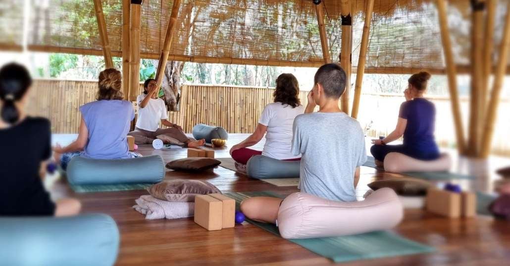 Group yoga class in wooden shala with woven bamboo walls and natural