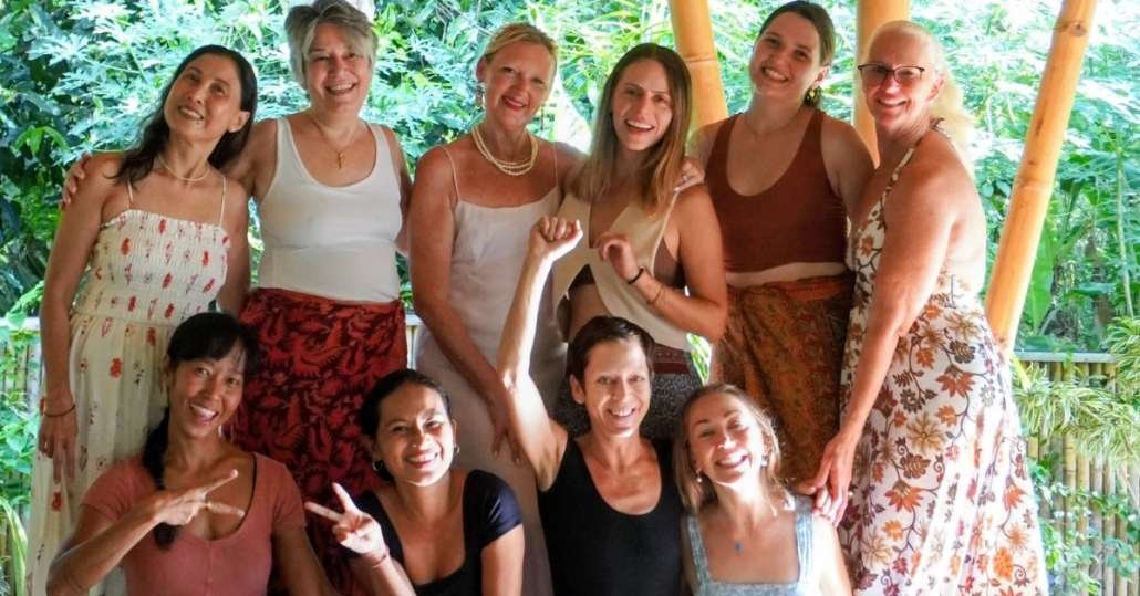 Group of ten women posing together in tropical yoga shala with bamboo