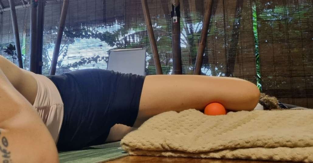 Student in supine position on sand with orange foam roller for myofascial