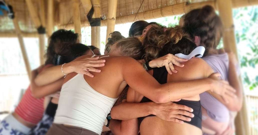 Group of students in close circle embrace under wooden pavilion with woven